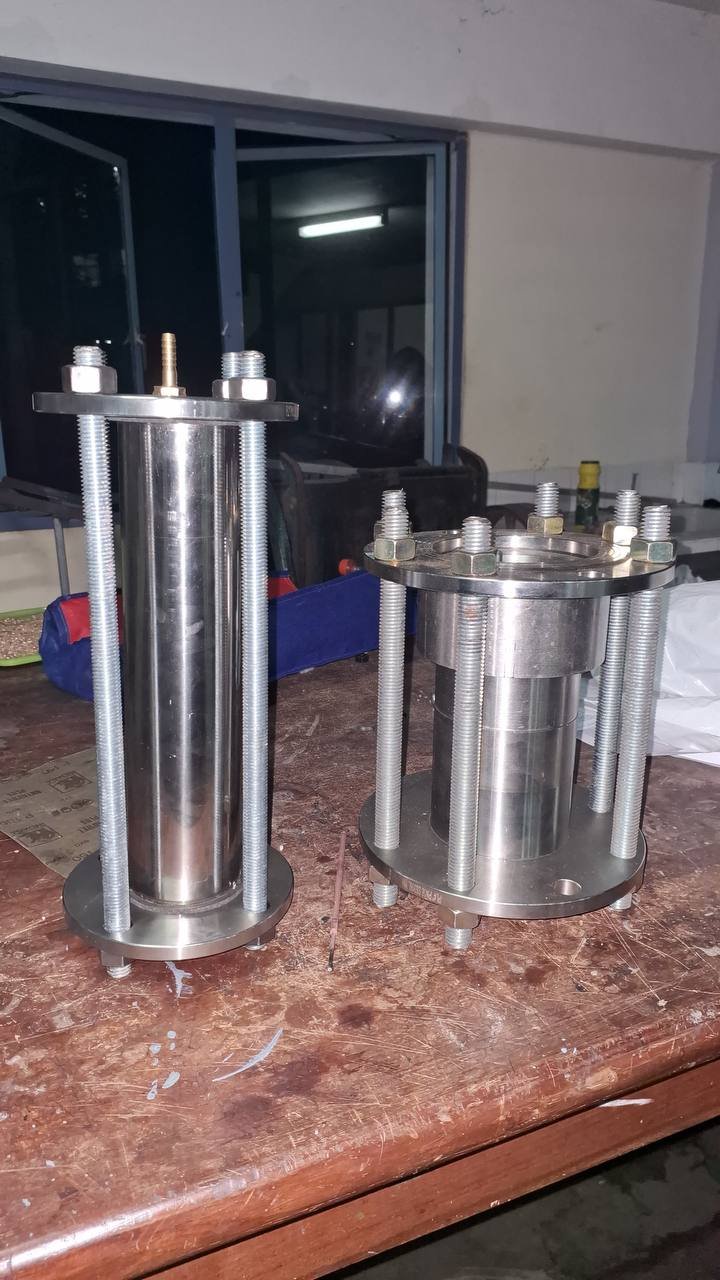 Two machined cylindrical Phoenix components with flanges and threaded tie rods on a workshop bench