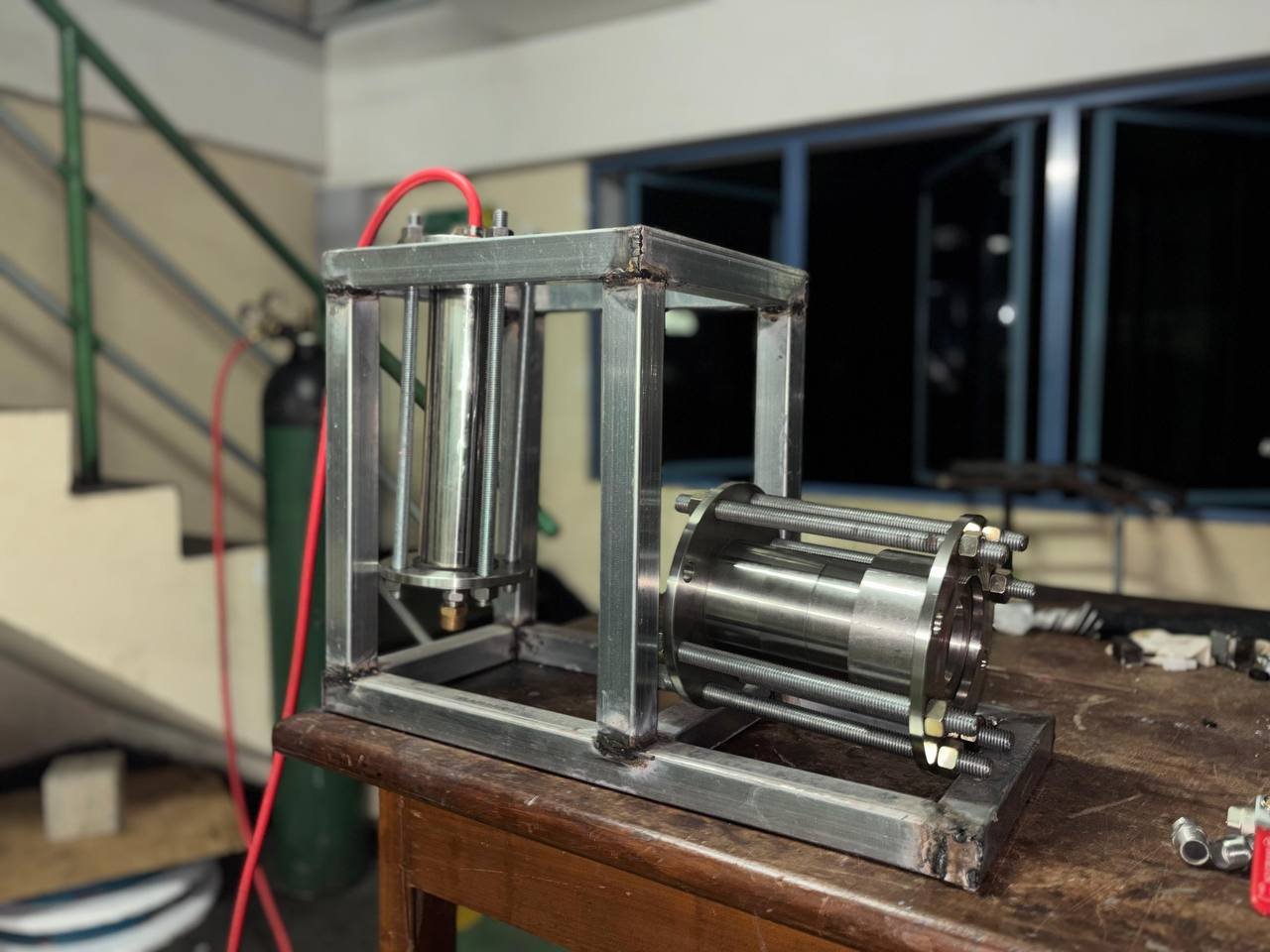 Fabricated Phoenix engine and vertical vessel mounted within a metal support frame on a workshop bench