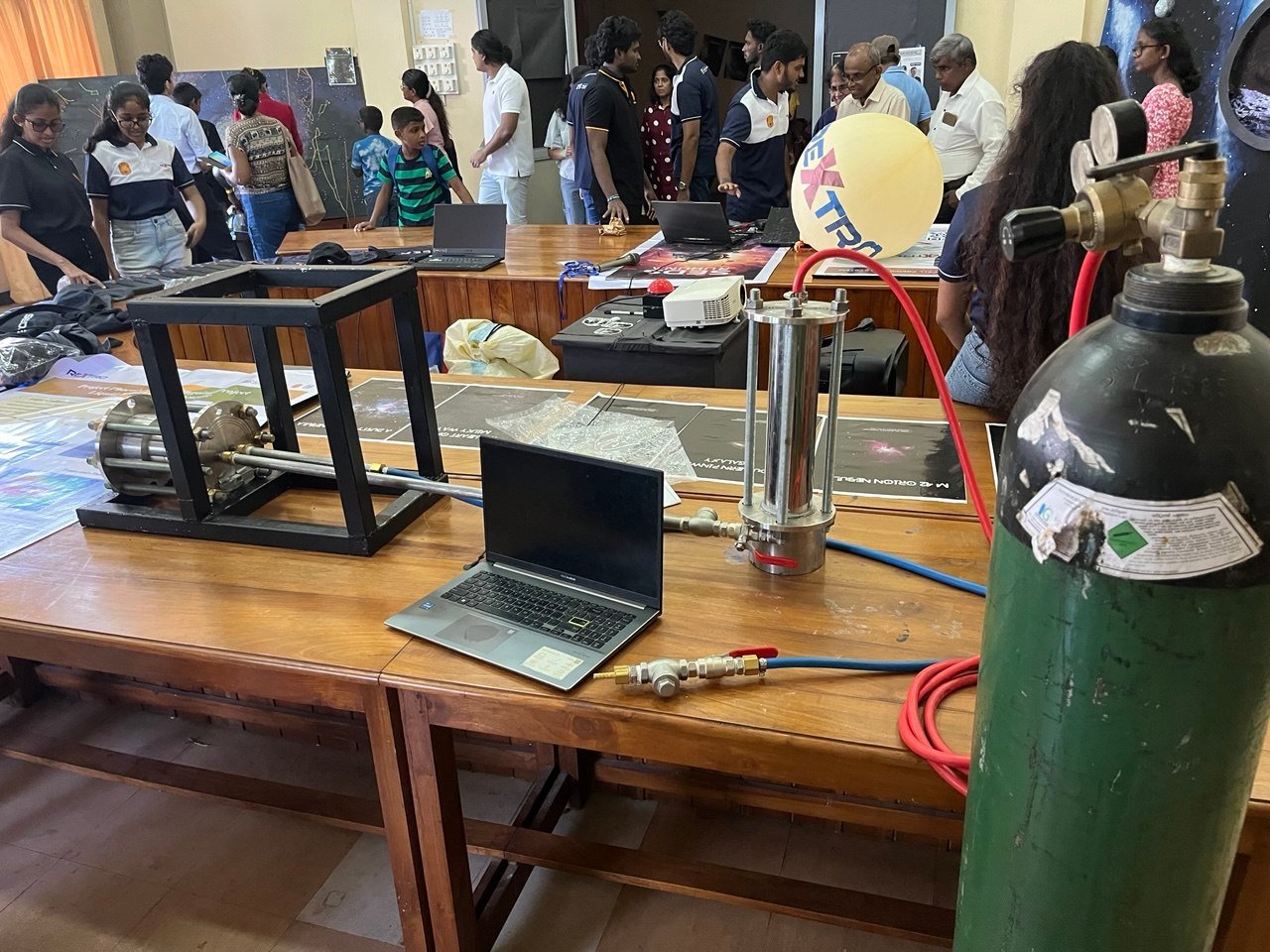 Phoenix project exhibition table with engine hardware, laptop, gas cylinder, and visitors